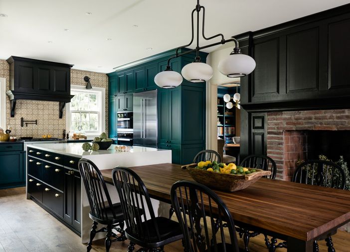 In the kitchen, cabinets by United Wholesale are painted a vibrant teal, and grounded with black accents, via the black pearl granite counters, Hudson Valley Lighting, stove hood, and fireplace surround. Rowland carried the patterned Ann Sacks tile to the ceiling, and specified reclaimed wood shelves to suspend over the windows, so everyday items are easily accessed. A large island covered in Upper Spectrum Maple White quartz cedes into a comfortable, custom seating area in front of the fireplace. Mafi wood flooring by Greenhome Solutions brings character.