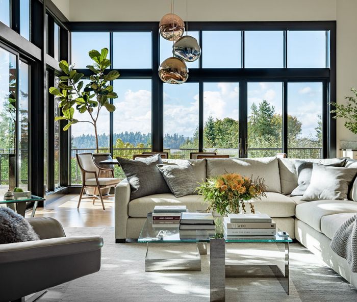 The living room is a light-filled sanctuary, thanks to tall windows and glass doors to the exterior deck, and an interior scheme by designer Colleen Knowles. The chic seating area has a J Redmond sectional and accent chair, the latter from Inform Interiors, around the Donghia coffee table. The Tufenkian Rug is from Driscoll Robbins. The dining room furniture is by McGuire, with statement-making Melt Pendants by Tom Dixon, also from Inform Interiors.