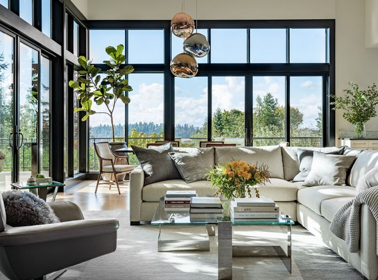 The living room is a light-filled sanctuary, thanks to tall windows and glass doors to the exterior deck, and an interior scheme by designer Colleen Knowles. The chic seating area has a J Redmond sectional and accent chair, the latter from Inform Interiors, around the Donghia coffee table. The Tufenkian Rug is from Driscoll Robbins. The dining room furniture is by McGuire, with statement-making Melt Pendants by Tom Dixon, also from Inform Interiors.