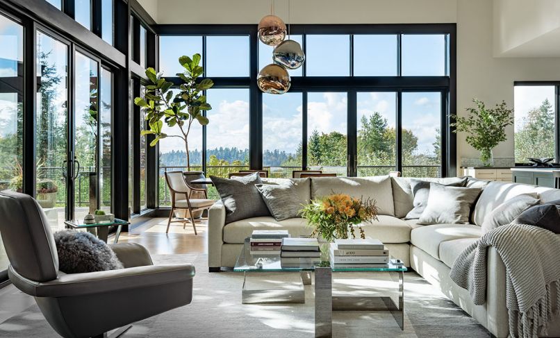 The living room is a light-filled sanctuary, thanks to tall windows and glass doors to the exterior deck, and an interior scheme by designer Colleen Knowles. The chic seating area has a J Redmond sectional and accent chair, the latter from Inform Interiors, around the Donghia coffee table. The Tufenkian Rug is from Driscoll Robbins. The dining room furniture is by McGuire, with statement-making Melt Pendants by Tom Dixon, also from Inform Interiors.