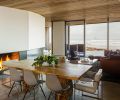 The wood covers the ceiling in the main room as well, and the exterior eaves, as seen through the windows from Portland Millwork. The floors are concrete with a radiant heat system underneath, and the metalwork at the fireplace is by Recychedelic. The paint throughout is Benjamin Moore. Freres designed the custom Oregon white-oak-and-brass table, and surrounded it with Eames side chairs and Milo Baughman armchairs, all from Design Within Reach.