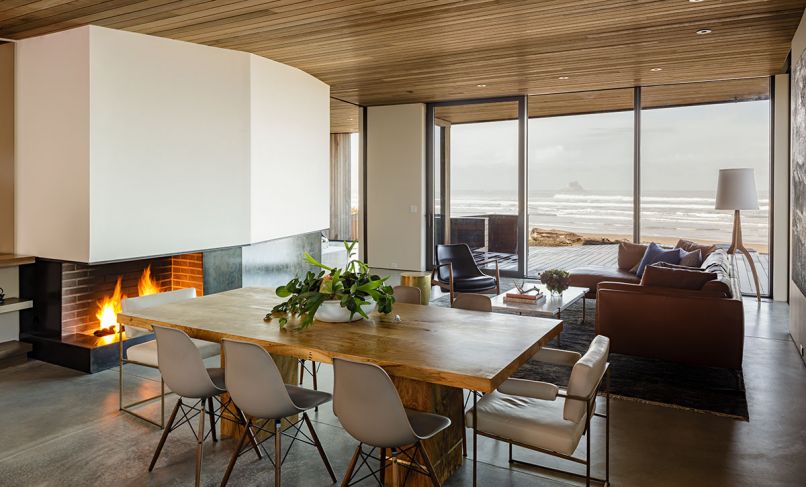 The wood covers the ceiling in the main room as well, and the exterior eaves, as seen through the windows from Portland Millwork. The floors are concrete with a radiant heat system underneath, and the metalwork at the fireplace is by Recychedelic. The paint throughout is Benjamin Moore. Freres designed the custom Oregon white-oak-and-brass table, and surrounded it with Eames side chairs and Milo Baughman armchairs, all from Design Within Reach.