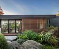 Grounded, organic sensibilities are reflected in the gardens and massing of the house. Natural stones from Marenakos Rock Center crop up against the split-levelled house trimmed in Blackened Cedar Open Rainscreen Siding from LS Cedar. E&H Construction created the clear cedar sliding screen on site. Chin designed the solid maple topped dining table left with kitchen and living room beyond. At right, up a half-story, is a guest bedroom.