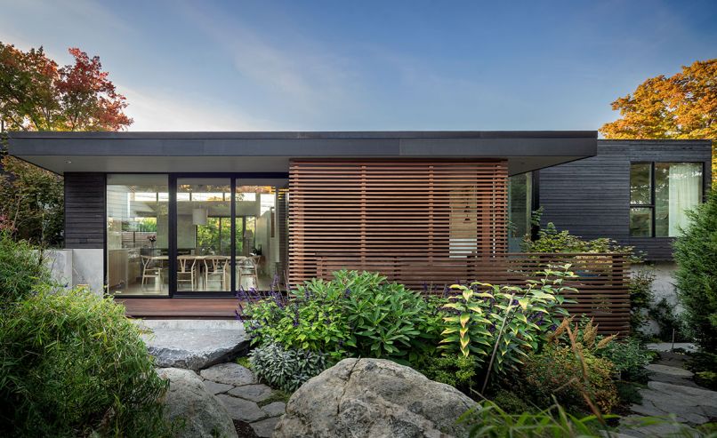 Grounded, organic sensibilities are reflected in the gardens and massing of the house. Natural stones from Marenakos Rock Center crop up against the split-levelled house trimmed in Blackened Cedar Open Rainscreen Siding from LS Cedar. E&H Construction created the clear cedar sliding screen on site. Chin designed the solid maple topped dining table left with kitchen and living room beyond. At right, up a half-story, is a guest bedroom.