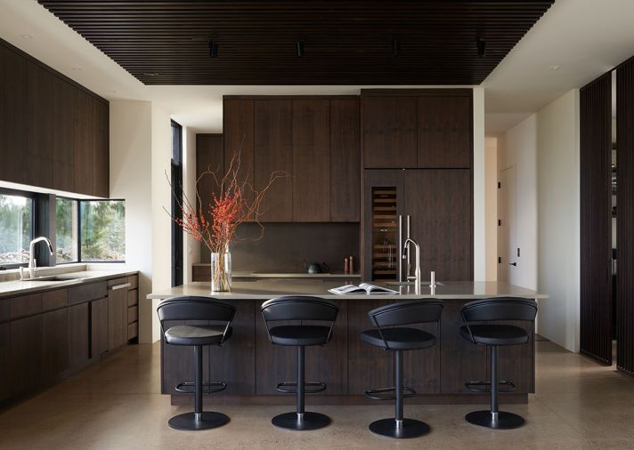 Poplar-stained wood screens define kitchen work area when mounted on ceiling and disguise ducting, speakers, and fire alarm system. Walnut-stained cabinetry and patina on steel backsplash reiterate elements found in living room. Connubia barstools hug quartz-topped island. Dornbracht sink faucets. Miele cooktop/induction oven. Faber, Inca Lux vent.