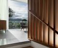 Free-floating walnut tread staircase flanked by slotted walnut screen and railing opens onto main living area with Italian stone flooring.