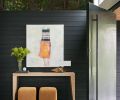 In the entry, a steel pivot door opens to a console table from Desiron NY, with a Blackman Cruz table lamp on top and Lee Industries poufs with suede by Keleen Leather. The artwork is by Chris Gwaltney.