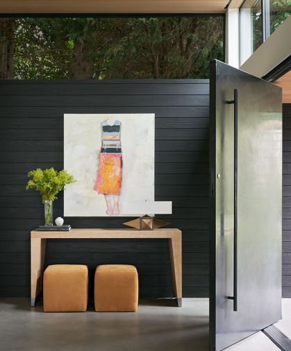 In the entry, a steel pivot door opens to a console table from Desiron NY, with a Blackman Cruz table lamp on top and Lee Industries poufs with suede by Keleen Leather. The artwork is by Chris Gwaltney.