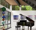 An alcove under the stairs overlooks a shade garden and is the perfect spot for the homeowners’ piano. A colorful series of paintings by Jaq Cartier complements a sculpture by Annie Morris.