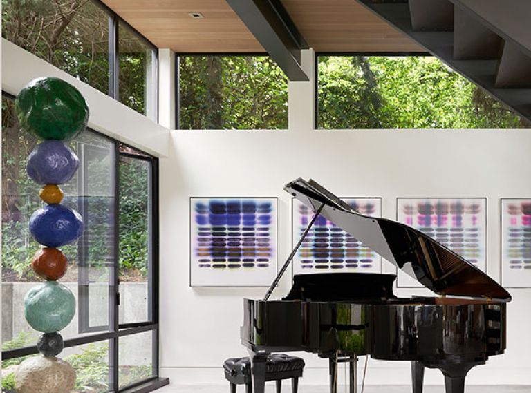 An alcove under the stairs overlooks a shade garden and is the perfect spot for the homeowners’ piano. A colorful series of paintings by Jaq Cartier complements a sculpture by Annie Morris.