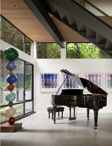 An alcove under the stairs overlooks a shade garden and is the perfect spot for the homeowners’ piano. A colorful series of paintings by Jaq Cartier complements a sculpture by Annie Morris.