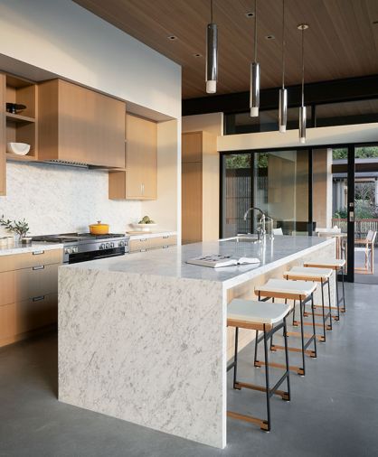 In the kitchen, sliding glass doors open the room to the covered outdoor space. The cabinetry was designed by Greg, whose parents had a kitchen cabinet business in Iowa, and built by Contour Woodworks. A Miele range, Dornbracht plumbing, Kelly Wearstler pendants, and Token barstools complete the scheme.