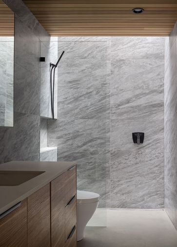 In the primary bathroom, porcelain tile called Marvel Stone Bardiglio wraps the walls. Leicht cabinetry forms the vanity, and the faucets are Brizo Vettis. The concrete floors have radiant heat.