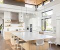 In the kitchen, white gloss upper cabinets and an opaque white glass tile backsplash from Contract Furnishings Mart are bright and modern. An extra-large island for casual family dining features elegant but durable Pental Quartz countertops and an additional prep sink.