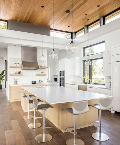 In the kitchen, white gloss upper cabinets and an opaque white glass tile backsplash from Contract Furnishings Mart are bright and modern. An extra-large island for casual family dining features elegant but durable Pental Quartz countertops and an additional prep sink.