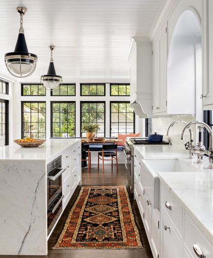 Dramatic Navy-blue pendants by The Urban Electric Co. spotlight Calacatta island. Custom corbel detail on range hood. Miele speed oven. Polished nickel Water Street Brass cabinet knobs from Chown Hardware. Driscoll Robbins Fine Carpets vintage rug reiterates Thos. Moser orange hued chair backs.