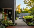 The custom, cast-in-place concrete pavers are a unique feature of this garden’s hardscapes. Formed, poured, and finished onsite, they lay a path to the front door but also step up to define the transition between niche areas of experience. Layered concrete walls obscure the road and driveway from the garden and create the sense of stepping into the house’s living areas while remaining outside. At the front door, modern mirrored orb hanging planters from CB2 add layers and light.