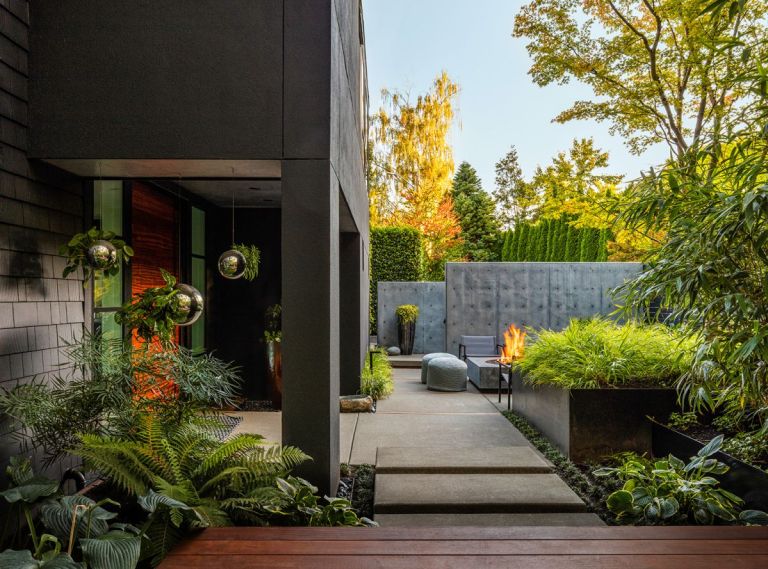 The custom, cast-in-place concrete pavers are a unique feature of this garden’s hardscapes. Formed, poured, and finished onsite, they lay a path to the front door but also step up to define the transition between niche areas of experience. Layered concrete walls obscure the road and driveway from the garden and create the sense of stepping into the house’s living areas while remaining outside. At the front door, modern mirrored orb hanging planters from CB2 add layers and light.