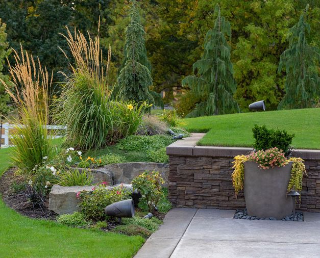 The homeowners take full advantage of their generous land, including adjacent horse and livestock pastures and barns, but the home lacked outdoor living space for entertaining and relaxing. Aerial views show how entertaining areas bring both intimacy and separation for large groups. Just past the pool deck, planters offer pops of color against natural stone retaining walls, while the addition of lush plantings soften hardscapes. Thoughtful lighting that adjusts with sunrise and sunset create a welcoming backdrop for evening gatherings.