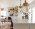 A pair of impressive Visual Comfort brass pendants add character to overall design and task lighting to the Carrara marble island countertop. Arteriors leather bar stools tuck beneath countertop. Coffee bar features Carrara marble backsplash crowned with high gloss handmade tiles. Floating wood shelves echo unseen wood end portion of adjacent island. Brass Rohl plumbing ties to Rejuvenation sconces. Sub-Zero beverage refrigerator.