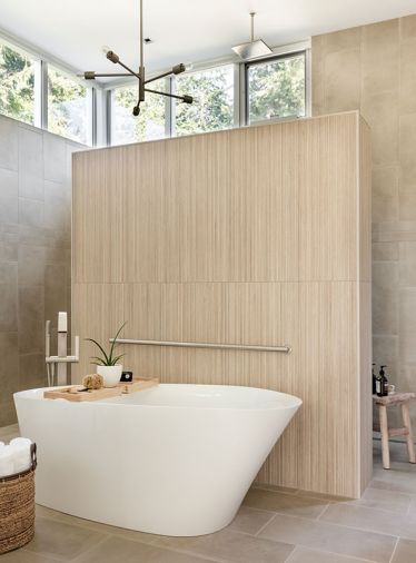 In the primary bathroom, the custom feature wall separating the soaking tub from the shower was built on-site, and wrapped in Porcelanosa Tile, Ice Nebraska in ‘Tea.’ The freestanding bath is a Kohler Veil from Keller Supply Kitchen & Bath Showcase, and above it, there’s a Livex Lighting branch light.