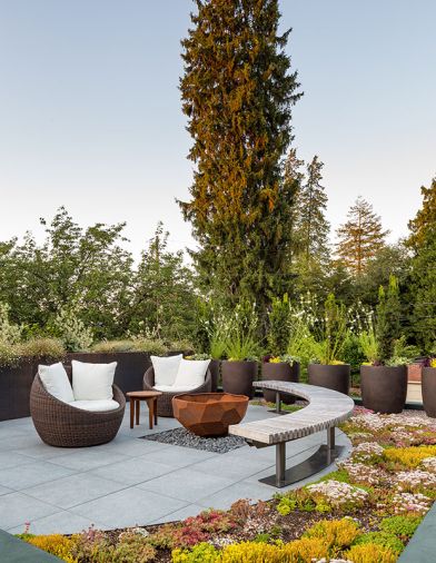 Furniture and planters are free-floating, including groundcover and sedums from Blooming Nursery styled on moveable trays. The pavers are a pedestal design that allows gas, lighting, and irrigation to flow hidden underneath. The planters cleverly hide the propane tanks for the firepit.