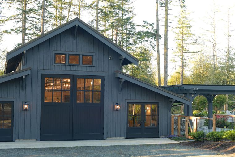 Dark Gray (Benjamin Moore “Cheating Heart”) swinging barn doors by Real Carriage Door Company mark the entrance to the party barn contrasting with Benjamin Moore “Stormy Sky” wood siding. Land Morphology’s pergola, right, features arched braces attaching to posts and painted to match the building.