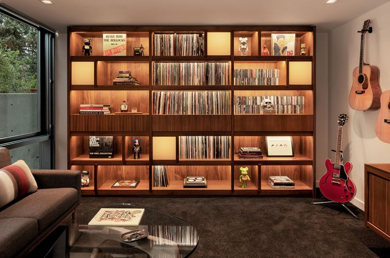 In the husband’s music room, the custom casework is designed by Katy Krider Interior Design, and built by OTL cabinetry. The design was inspired by the clients’ travels to Tokyo and carefully detailed to accommodate an extensive vinyl, CD, and book collection. Backlit shoji-paper screens foster an ambient glow.