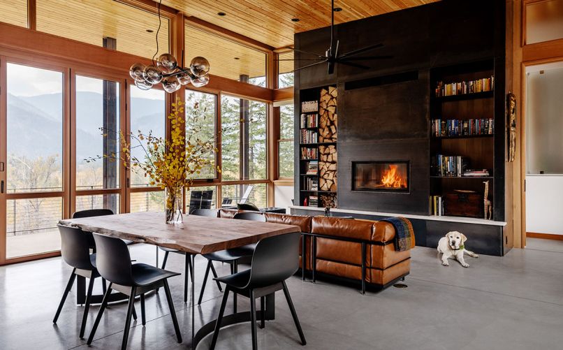 The focal point of the great room is the dramatic fireplace wall, flanked by wood storage and bookshelves. An insert from Wittus – Fire by Design is surrounded by site-built hot-rolled steel from Johnsen Steel Works. An Eternity Modern sofa sits beneath a Minka-Aire Extreme H2O Ceiling Fan. In the dining room, a Bent Dining Table from Moe’s Home Collection is surrounded by Hay chairs.