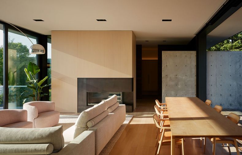 The fireplace column is wrapped in rift-cut white oak veneer panels that are grain-matched for an unbroken effect. The cast concrete wall from Fieldworks Custom Concrete continues inside, and down to the basement. The bespoke dining table is by Dovetail, and surrounded by Maruni chairs from Inform Interiors.