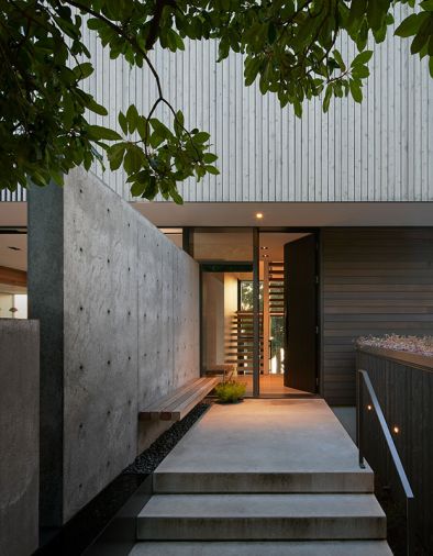 The “outdoor vestibule” includes a concrete path leading to the stained Sapele door with a hammer-formed brass pull by Dovetail. A floating Western red cedar bench is a place to pause, and the channel of river rock underneath extends into the foyer.