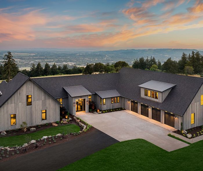 Wrapping the rustic “Hewn” Napa Valley inspired home in Hewn grey cedar siding sets it against lush green landscape and native northwest plantings. Custom double entry doors lit by gas burning lanterns open onto great room with panoramic vista. Black trimmed Marvin windows from Parr Lumber echo four-car garage doors. EV charging station.