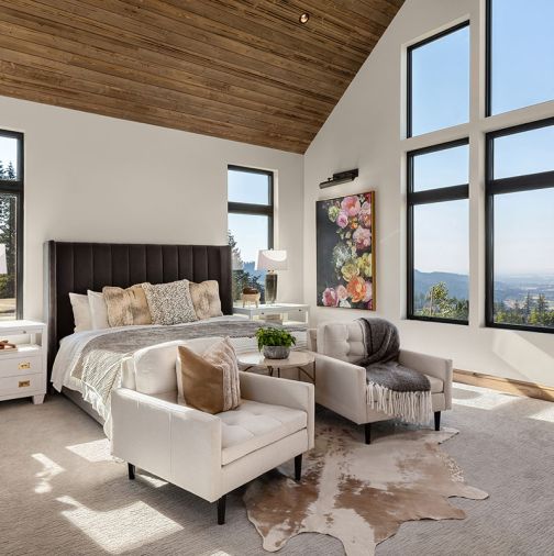 The East Wing full ensuite guest bedroom’s “story” features gathered elements from worldly travels, including the Old-World style painting from ArtworxLA, echoing the Essentials for Living dark truffle gray channeled headboard. New Pacific Direct chairs provide comfort for TV viewing.