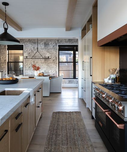 The dining room has Cole and Son wallpaper from Kravet, and chairs from Rejuvenation. A Sub-Zero designer series fridge is concealed with a cabinet front, while nearby, both the BlueStar range and custom hood vent have copper accents. All kitchen appliances were sourced from Eastbank Contractor Appliances.