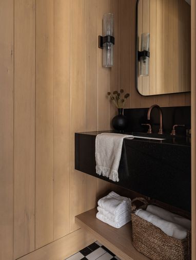 The powder room is encased in white oak tongue and groove paneling installed by Stoneridge Custom Development, with a Negresco leathered granite from Bedroasians. The sconce is by Arteriors.