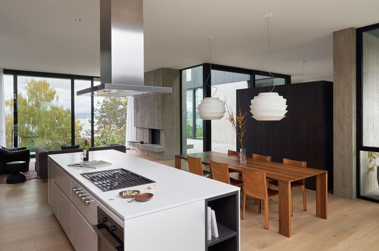 Leicht Seattle brought German-built and engineered kitchen components to nest seamlessly within the open, vaulted living space. The white Neolith island and countertop evoke an altar to cuisine. The range is Wolf, additional appliances are Miele. Ceiling lighting throughout is from Seattle Lighting. The Cassina dining chairs from the owner’s collection perfectly match the Bensen Radii dining table from Inform Interiors.