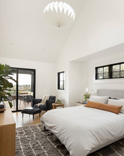 In the primary bedroom, a new slider from Parr Design Center connects the room to the expanded deck. Vaulted ceilings increase the sense of space. The Adrian Dresser and nightstands, Ella bed, Matteo Chair and Ottoman, and Orikata Saucer Pendant are all from Room & Board.