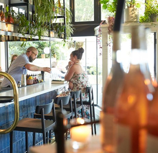 The bar is defined by a custom steel beverage rack packed with leafy plants and natural wine. “It was created to showcase the ever-changing wine list, and the plants add a lush layered look,” says Holly Freres.