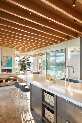 The upper floor has polished concrete flooring with radiant heating throughout, with overhead lighting by Kichler Lighting tucked into the fir and cedar ceiling. The kitchen bar stools are custom by Garret Cord Werner Architects and Interior Designers. The clean design and natural light create an airy, welcoming space.