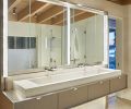 In the primary bathroom, Mercer Builders made a custom mirror cabinet on-site with opaque glass light from Stephen Hirt and glass from Distinctive Glass. The custom floating vanity features a stone basin sink atop a stainless-steel bar counter.