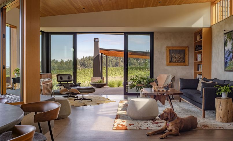 Integrated glass sliders from Portland Millwork open the indoor living to the outdoor patio. The primary living area is outfitted with an Emmy Sofa in Walnut & Cinder Pebble Weave, a Paulistano Armchair, Herman Miller Eames chair and a custom table by Fallen Industry.