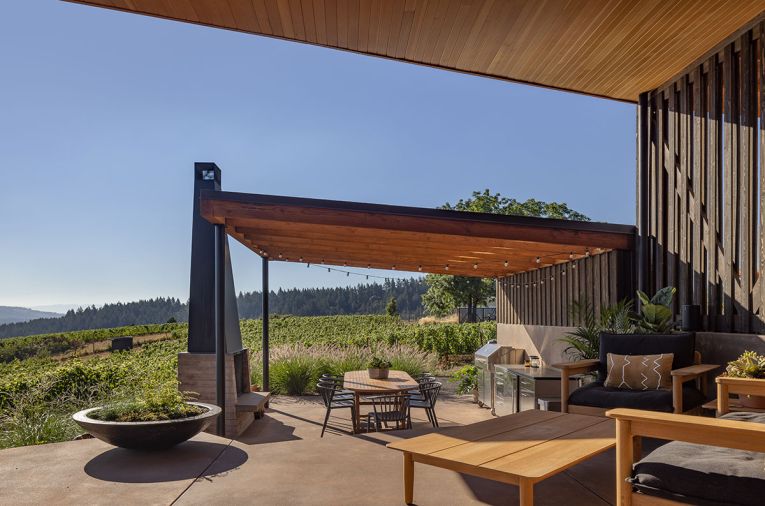 Hammer & Hand site-built the outdoor fireplace, mounting a custom steel chimney on a board-formed concrete firebox. The Terassi series teak outdoor furniture contrasts with the darker stained western red cedar siding from Lakeside Lumber and Benjamin Moore.