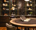 The downstairs whiskey bar has custom shelving by Forsyth Metal Works joined with black wall tile, a game table by Burke Decor, and chairs from Four Hands.