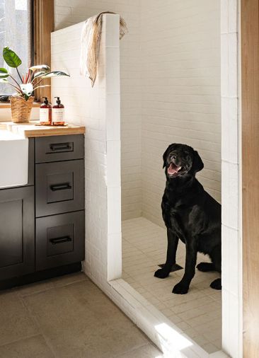 In the laundry room, Nellie doesn’t mind bathtime as she checks out the limestone floors and custom butcher block counters by WoodRidge Custom Homes.