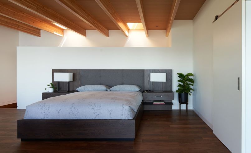 In the primary bedroom, operable skylights over the staircase circulate air and bring in light. The bedside lamps are from Seattle Lighting, while the walnut flooring is from California Hardwoods.