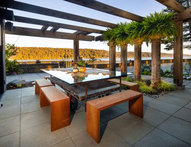 In the outdoor dining room, four columns border a patio composed of Vancouver Bay Architectural Slabs from Mutual Materials. Jane Friedman made the custom glass table from an old factory cart.