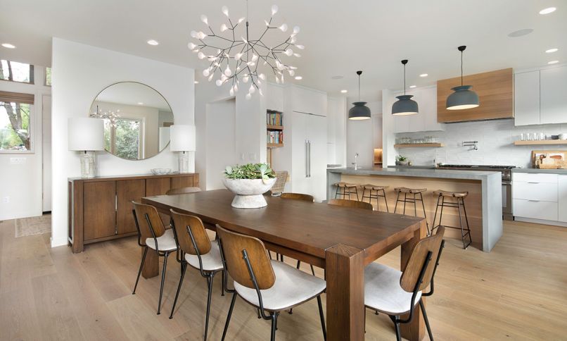 In the dining room, Visual Comfort Pastiche Large Table Lamps from Harper House Design sit atop a buffet. Four Hands Jared Dining chairs from Harper House Design surround the dining table, lit by the Bertjan Pot for Moooi, Heracleum II chandelier from DWR.