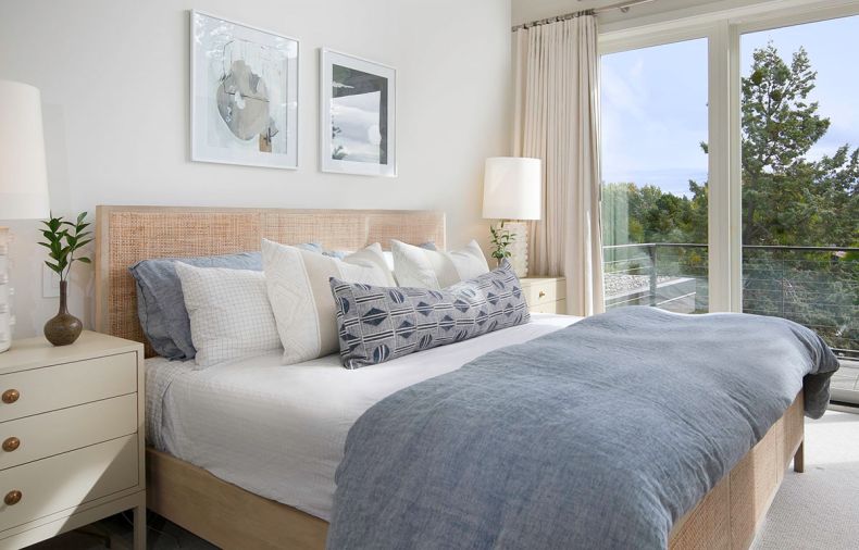 Artwork by Allie Blanchard hangs above a wood bed with caned insets from Four Hands. The nightstands are from Chelsea Textiles.