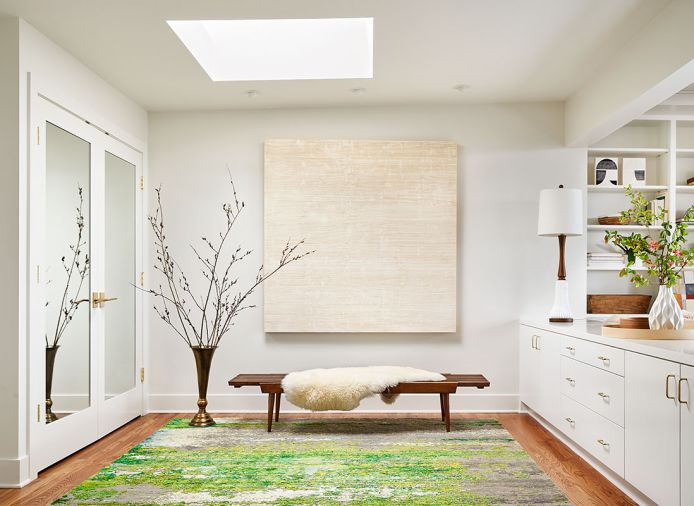 Rockwood Cabinetry created the credenza that divides the contiguous spaces. The newly added closet, left, is handsomely adorned with Culver Glass doors. Christiane Millinger rug reiterates Falvey’s passion for green. An Urbanite lamp rises gracefully toward Madeline Shinn Boyle’s “Fields” artwork.
