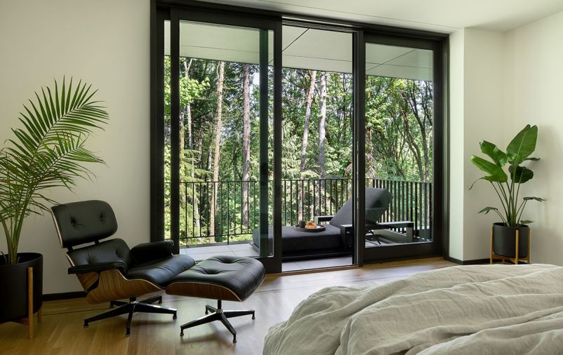 In the primary suite, glass doors slide open to a private balcony. The walls throughout are William / Kaven White from Sherwin-Williams. A Herman Miller, Eames Lounge Chair and Ottoman from DWR sits to the side.